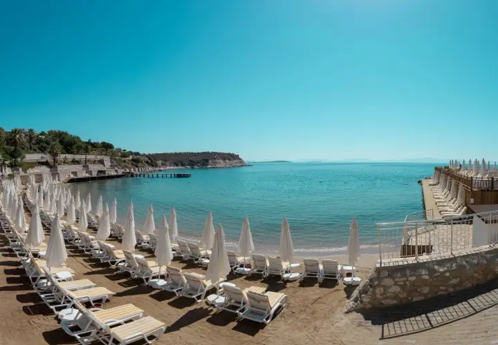 Plaża z rzędami leżaków i parasoli w Anadolu Hotels Didim Club. Błękitne morze i spokojne niebo zapraszają do relaksu.