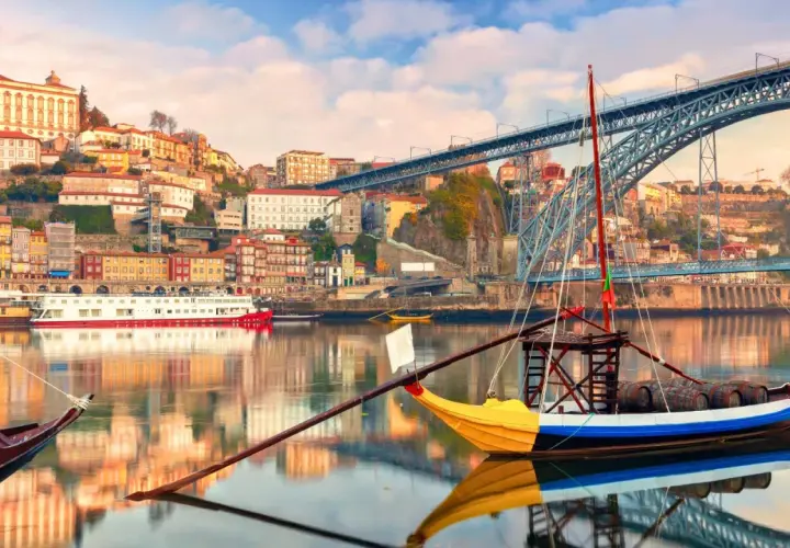 Barcos tradicionales navegan por el río Duero, con la colorida Ribeira y el puente Dom Luís I al fondo. Perfectas rutas cerca de Oporto para explorar.