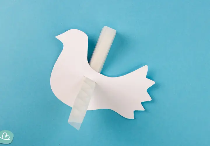 Eine weiße Papier-Friedenstaube wird mit Klebeband befestigt. Bastelanleitung für eine Friedenstaube.