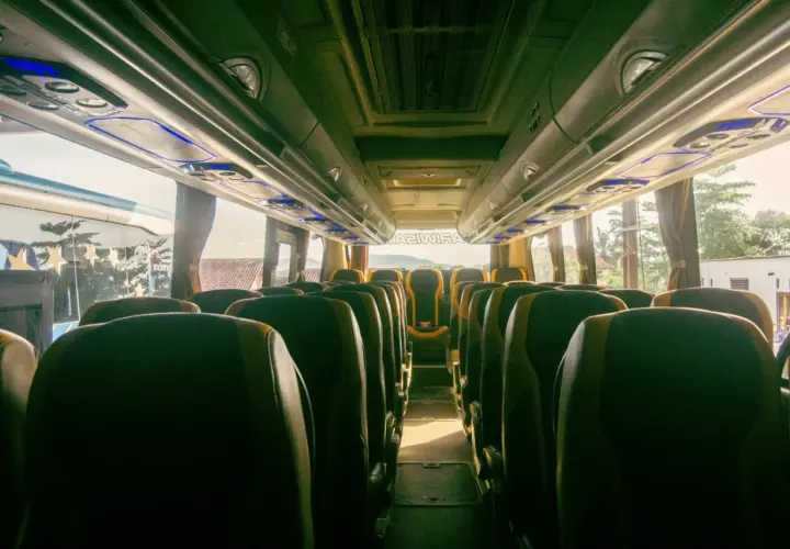 Wnętrze autobusu z rzędami ciemnych siedzeń i niebieskim oświetleniem podsufitowym.