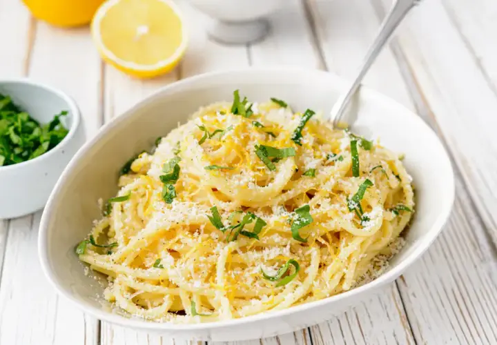Un plat de pâtes au citron, garni de persil frais et de parmesan râpé, prêt à être dégusté.