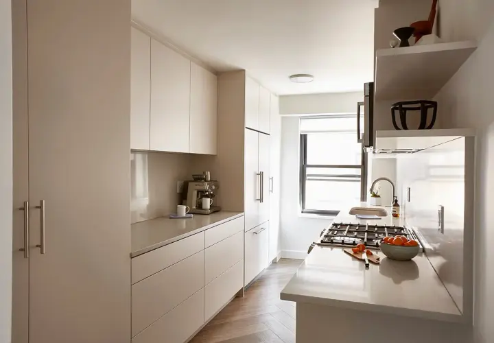 A modern galley kitchen makeover featuring sleek, handleless cabinets, a coffee machine, and a gas stove with a bowl of oranges.