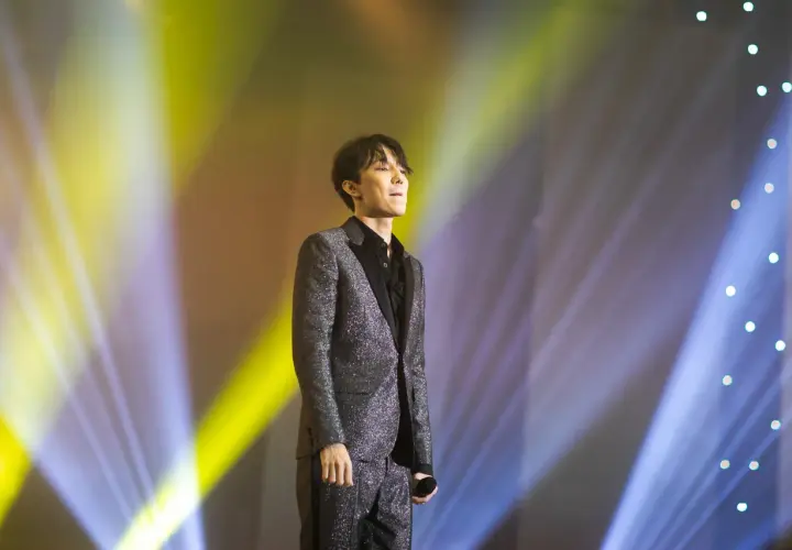Dimash Kudaibergen w błyszczącym garniturze na scenie, w świetle reflektorów. Jego życie prywatne pozostaje tajemnicą.