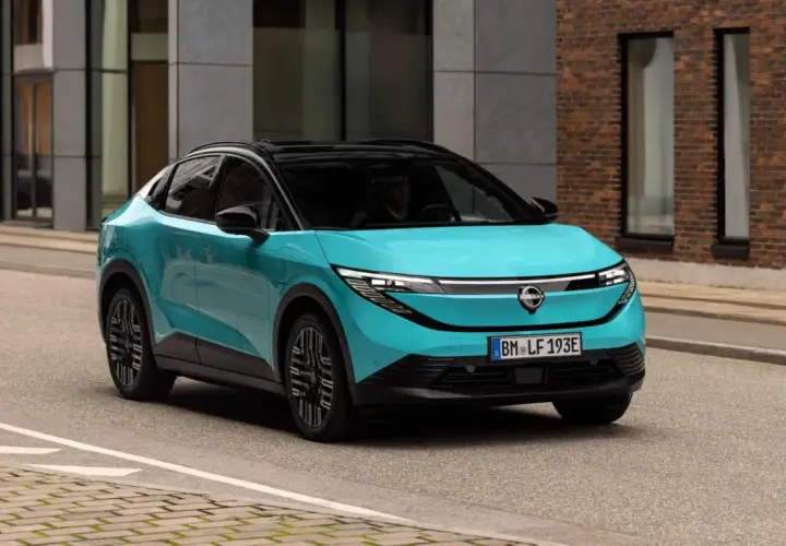 La Nissan Leaf 2026, in un vivace color acquamarina, sfreccia su una strada urbana, con un design futuristico che cattura l'attenzione.