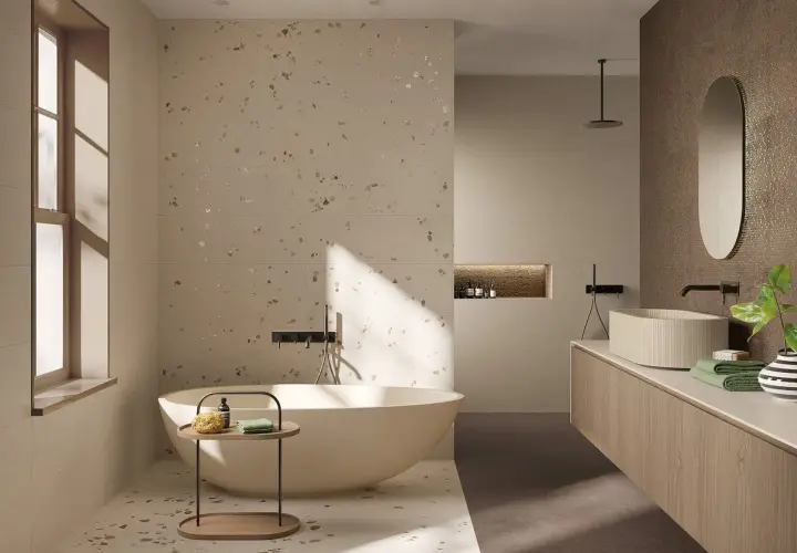 Bagno moderno con vasca freestanding e lavabo su mobile sospeso. Pareti e pavimento in fap gres porcellanato effetto terrazzo con inserti metallici.