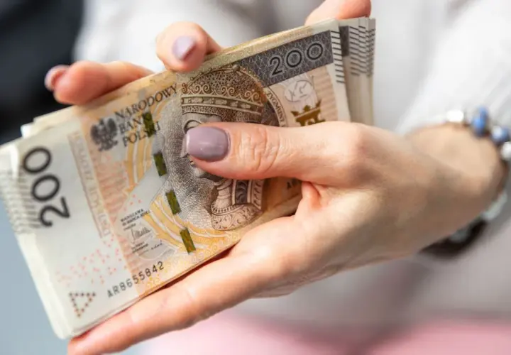 Dłonie trzymające stos banknotów 200 zł. Czas oczekiwania na wypłatę emerytury po złożeniu wniosku.
