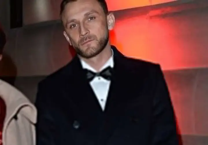 Kamil Nożyński z partnerką na ściance. Elegancki garnitur i czerwona sukienka.