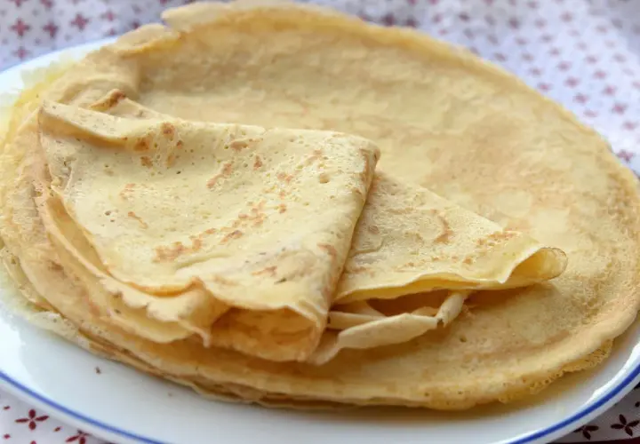 Stos cienkich, złocistych naleśników bez mleka, ułożonych na białym talerzu. Idealne na śniadanie lub deser.