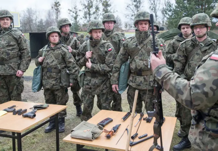 Żołnierze w mundurach ćwiczą, co zabrać na ćwiczenia rezerwy. Na stołach broń, magazynki, nóż i torby.