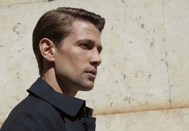 Hombre con corte de pelo con raya, peinado hacia atrás con gel, luciendo elegante y moderno.