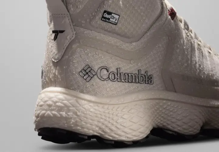 Close-up of a beige Columbia hiking boot with water droplets. The boot features the Columbia logo and "OutDry WATERPROOF" branding, showcasing its durable, water-resistant design.