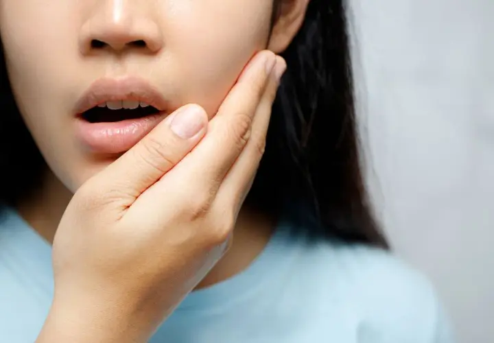 Mujer con mano en la mejilla, experimentando dolor de dientes al quitar Invisalign.