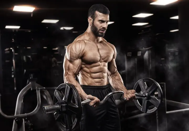 Mężczyzna z wyrzeźbionymi mięśniami wykonuje ćwiczenia na biceps z łamaną sztangą w siłowni.