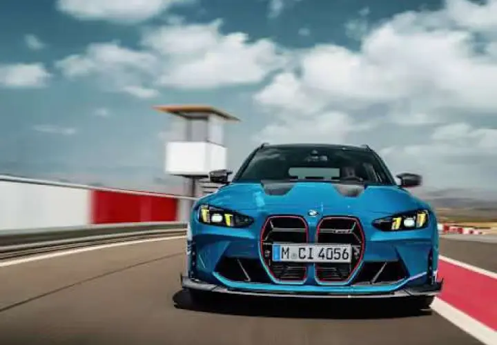 Niebieskie BMW M3 Competition pędzi po torze wyścigowym, chmury na niebie dodają dynamiki.