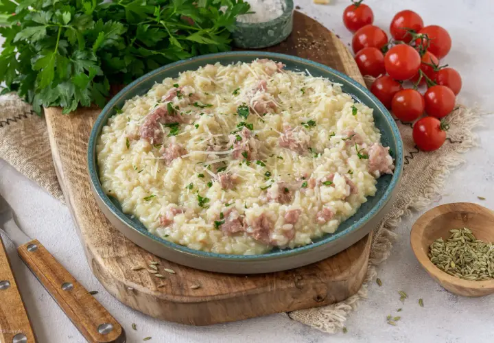 Cremiges Risotto mit Salsiccia, garniert mit Parmesan und Petersilie, serviert auf einem rustikalen Holzbrett.