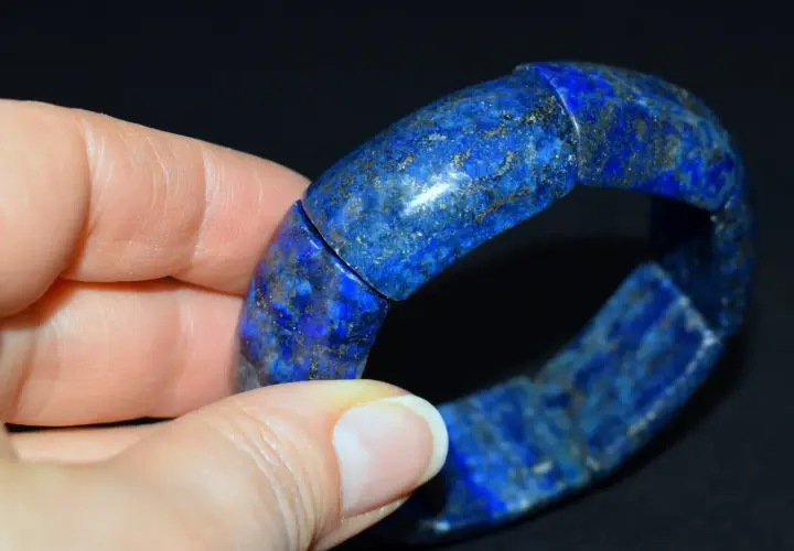 Dłoń trzyma bransoletkę z lapis lazuli, kamienia o intensywnym niebieskim kolorze i złotych inkluzjach.