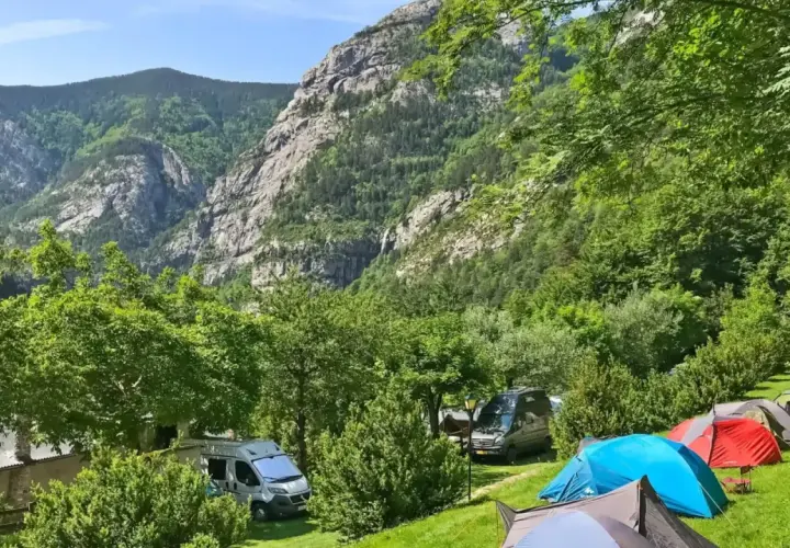 Acampar en este valle es una experiencia de los mejores camping. Tiendas de campaña y furgonetas aparcadas en un prado verde, con imponentes montañas boscosas de fondo.