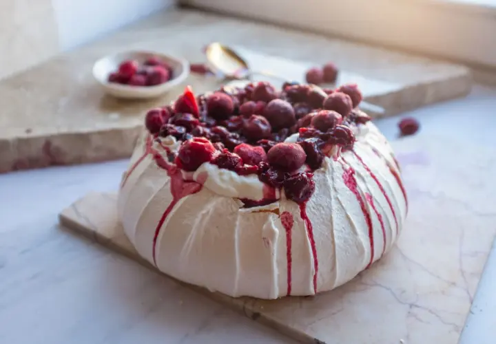 Pyszny tort pavlova z bitą śmietaną i wiśniami, ozdobiony krwistoczerwonym sosem.