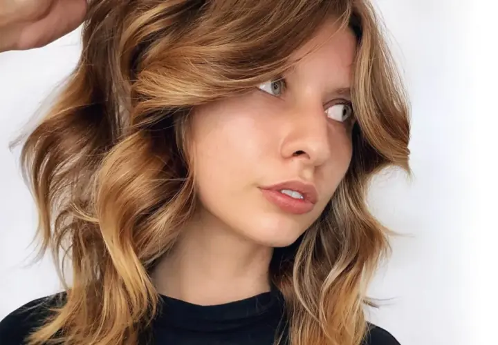 Mujer con cabello castaña iluminada, con ondas suaves y reflejos dorados que resaltan su rostro.