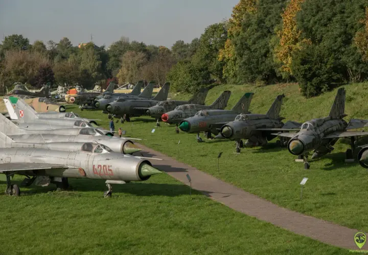 Samoloty wojskowe na trawie w Muzeum Lotnictwa w Krakowie. Widać myśliwce MiG-21 i inne maszyny.