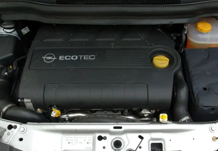 Silnik Ecotec w Oplu Zafira B. Widoczny czarny plastikowy dekiel z logo Opla i napisem Ecotec, żółty korek oleju i zbiorniczek płynu chłodniczego.