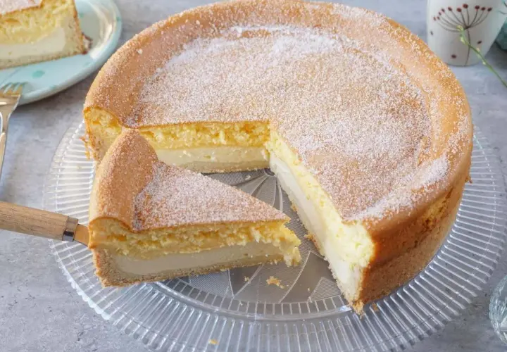 Saftige eierschecke ohne boden, mit Puderzucker bestäubt, auf einem Tortenteller. Ein Stück wurde bereits herausgeschnitten.