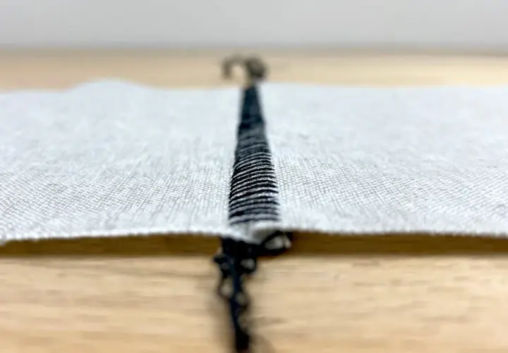 Close-up of a black stitch on white fabric, showing the difference between flatlock and coverstitch techniques.