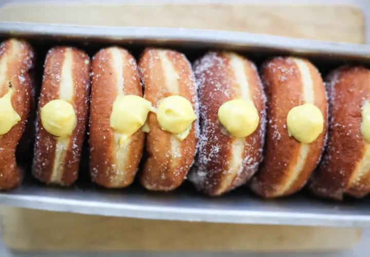 Una fila di bomboloni alla crema, cosparsi di zucchero, pronti per essere gustati.
