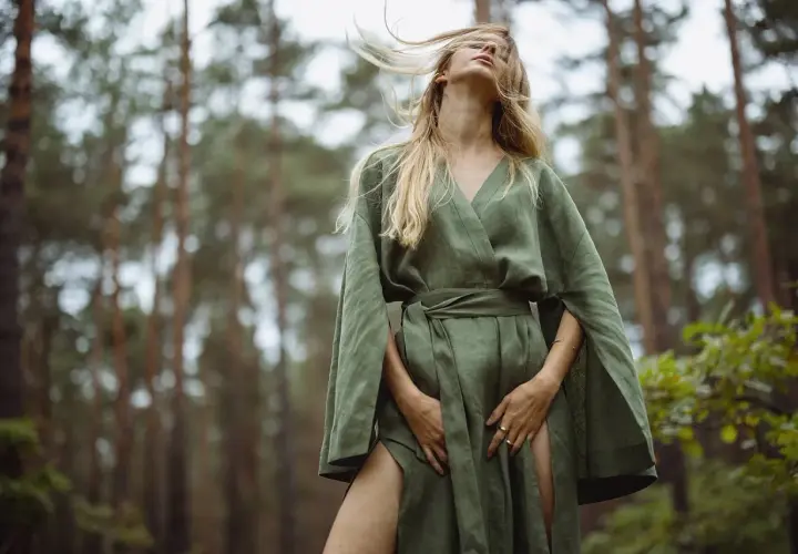 Kobieta w lnianej sukience w lesie. Włosy rozwiane przez wiatr, zmysłowa fotografia mody.
