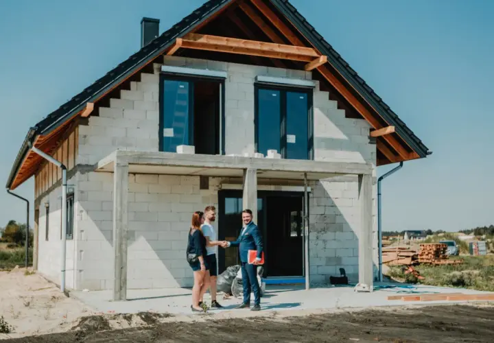 Para młoda wita się z doradcą finansowym przed budowanym domem. Marzenie o własnym gniazdku staje się realne dzięki kredytowi na budowę domu.