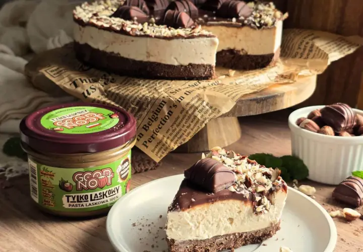 Ciasto Kinder Bueno bez pieczenia: kawałek na talerzu, obok słoik pasty orzechowej i orzechy.