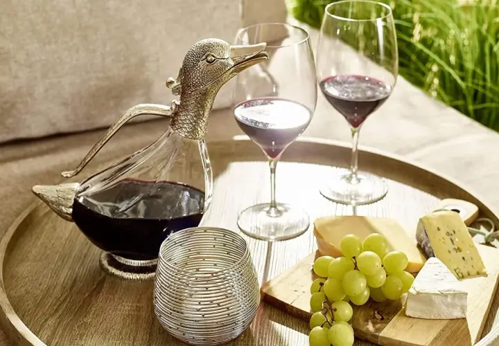 Dekantiert bedeutet, Wein in eine Karaffe zu füllen, um ihn zu belüften. Hier: ein Entenkaraffe mit Rotwein, Gläser, Käse und Trauben.