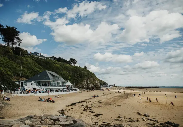 Plage normande avec restaurant en bord de mer, gens sur le sable et terrain de volley.