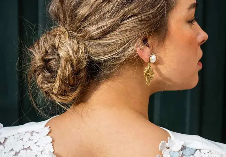 Elegante recogido pelo rizado boda invitada, con un moño trenzado y pendientes dorados.