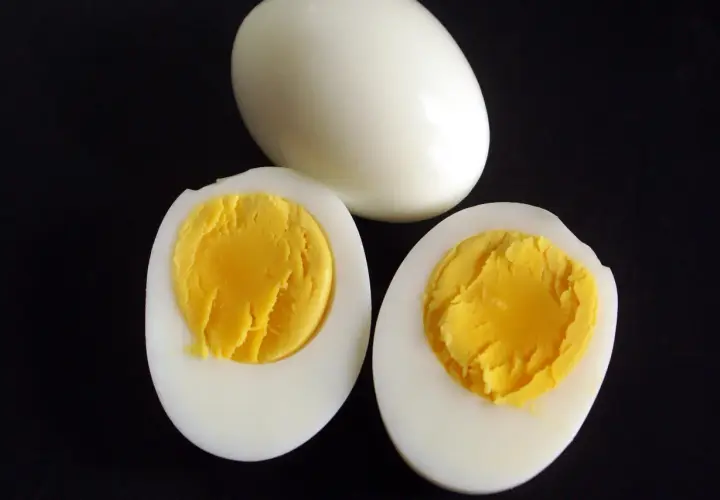 Un œuf entier et deux moitiés d'œufs durs sur fond noir, montrant le jaune bien cuit. Parfait pour une salade ou un en-cas.