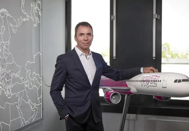Mężczyzna w garniturze stoi obok modelu samolotu Wizz Air, z mapą Europy w tle.