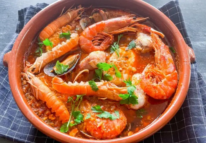 Deliciosa zarzuela de pescado con gambas, mejillones y cigalas en una cazuela de barro, decorada con perejil fresco.