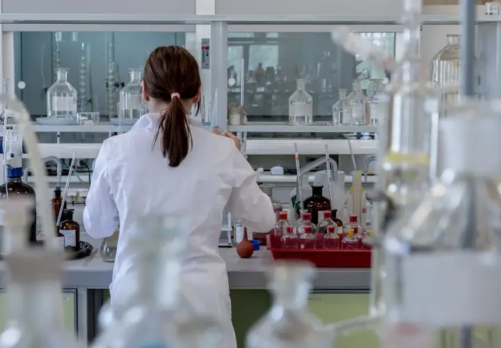 Naukowczyni w białym fartuchu pracuje w laboratorium, otoczona szkłem laboratoryjnym. Analizuje próbki, być może badając rdw-cv.