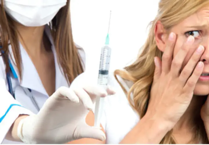 Una donna con espressione di paura degli aghi, copre il viso mentre un'infermiera con guanti bianchi tiene una siringa.