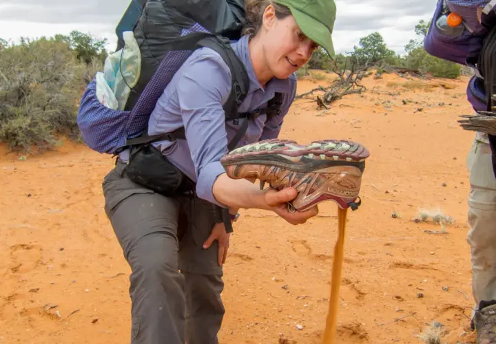 A hiker shakes sand from a shoe, demonstrating the challenge of finding the best shoes for hiking in sand.