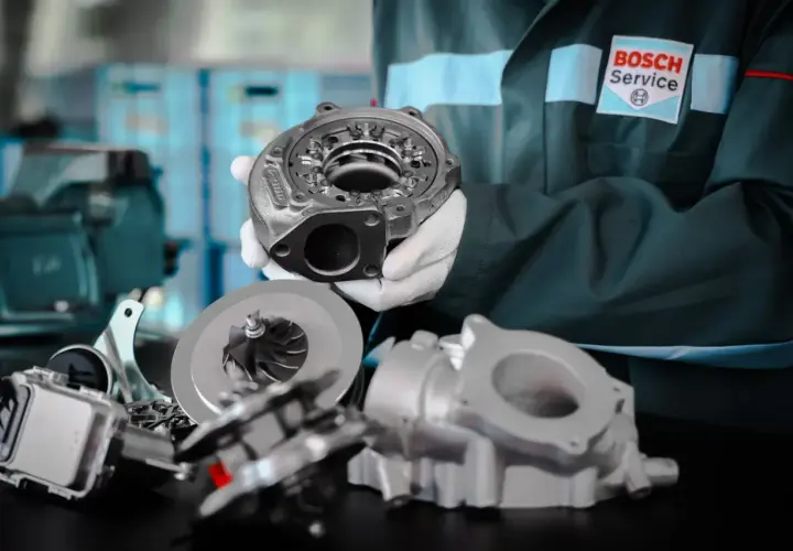 Mechanik w białych rękawiczkach prezentuje części turbosprężarki, pokazując jak sprawdzić turbinę w dieslu.