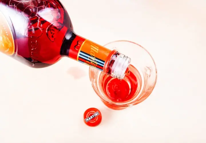 Nalewanie czerwonego Martini Fiero drinka do szklanki. Obok leży czerwona zakrętka z logo Martini.