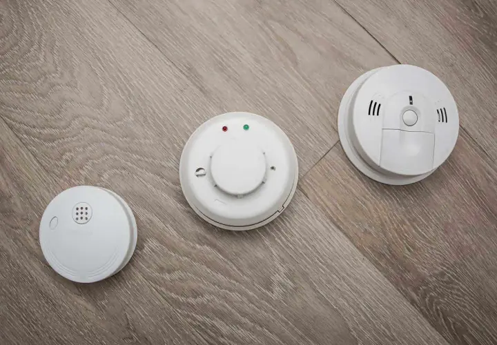 Trois détecteurs de fumée blancs sur un parquet. L'obligation d'installer un détecteur de fumée en entreprise est une mesure de sécurité essentielle.