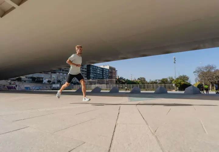 Mężczyzna w lekkim ubraniu biegnie pod betonowym zadaszeniem, realizując swój plan treningowy bieganie 10 km.