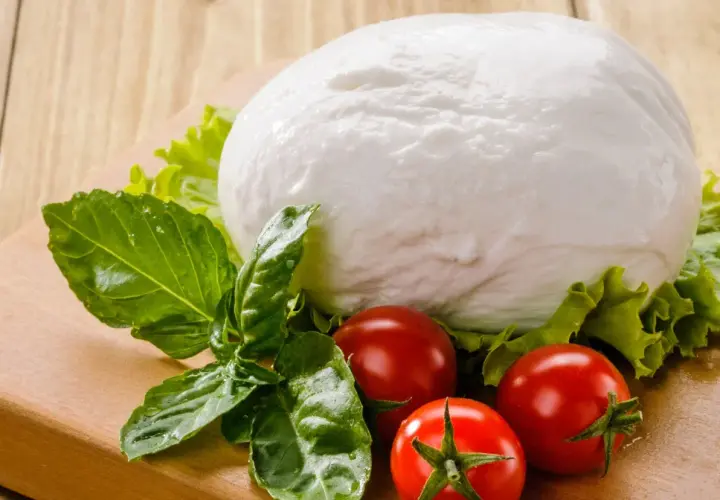 Kulista mozzarella, pomidorki i bazylia na desce. Czy mozzarella ma dużo białka? Tak, to świetne źródło białka!