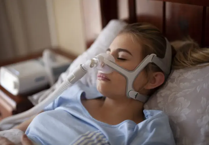 Kobieta śpi z maską CPAP, która pomaga na bezdech senny. Urządzenie zapewnia spokojny oddech przez całą noc.