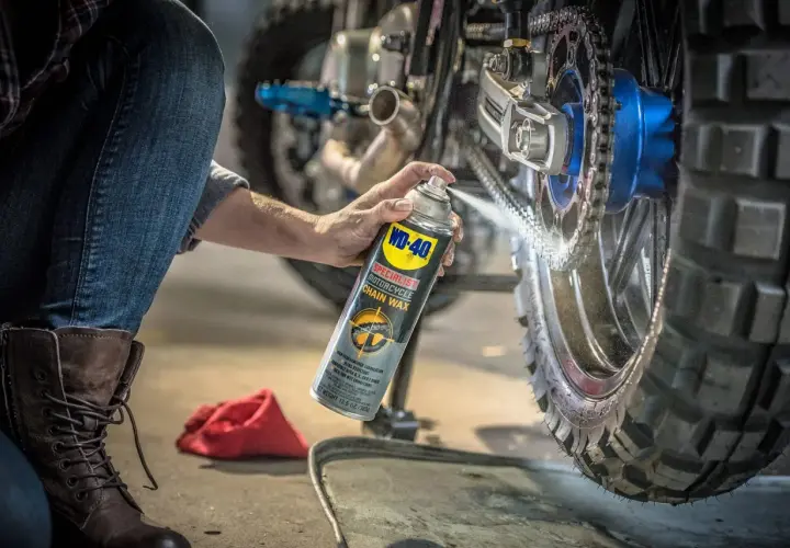 Persona en cuclillas engrasa cadena moto con spray WD-40.