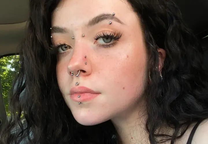 Dziewczyna z wieloma kolczykami, w tym kolczyk w brwi, septum i na ustach.