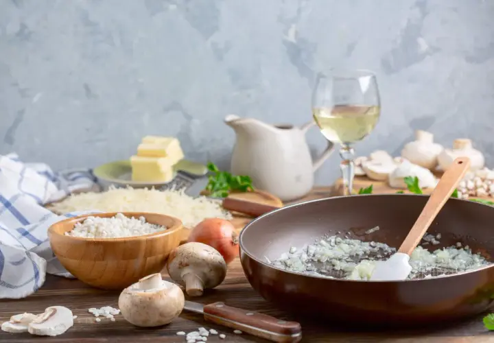 Préparation d'un risotto aux champignons, avec riz, oignons, champignons, parmesan, beurre et un verre de vin blanc.