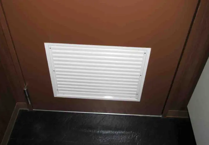 Griglia di ventilazione bianca su porta marrone, ideale per capire come arieggiare una stanza senza finestre.